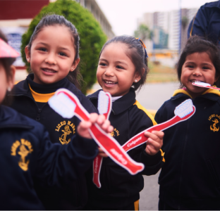 Two young girls in uniform mimicking toothbrushing with carboard brushes