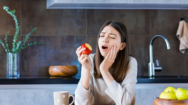 Woman with tooth pain eating an apple