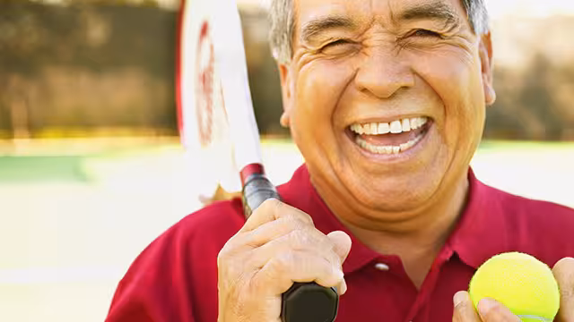 man smiling holding tennis ball and racket